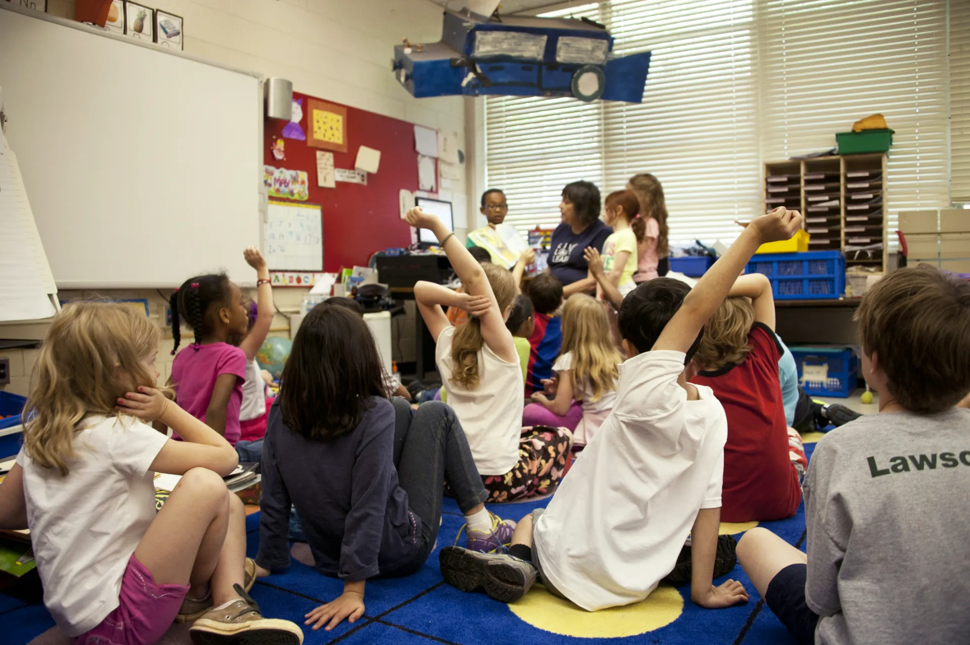 students sitting on ground and raising their hands